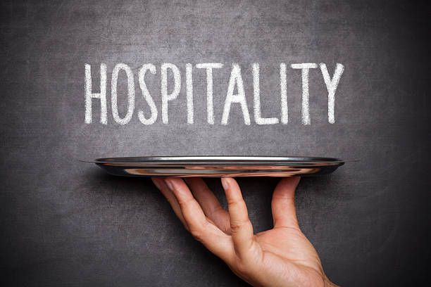 hand holding silver tray with word ,, hospitality'' written on blackboard